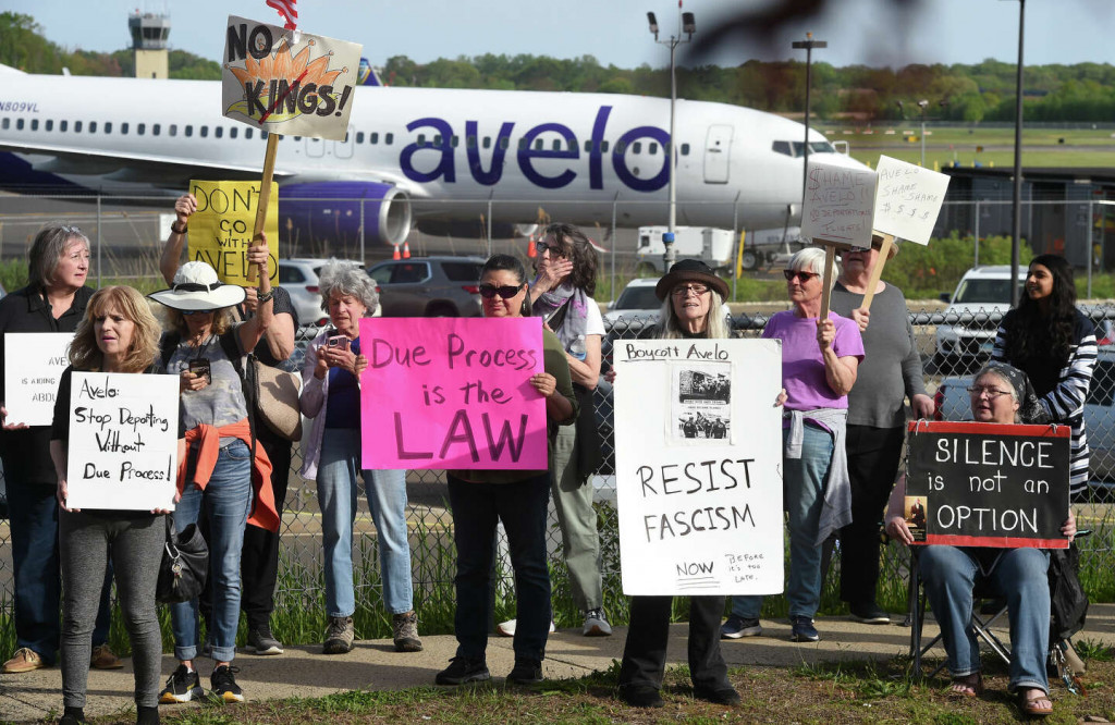 Protesters with signs saying "Resist fascism" in front of an Avelo plane.